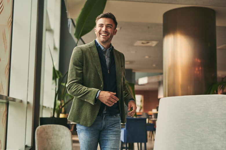 Man walking in a hotel lobby with a green corduroy jacket.
