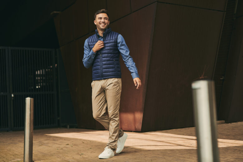 Man wearing a dark blue bodywarmer, ready to unzip it. 
